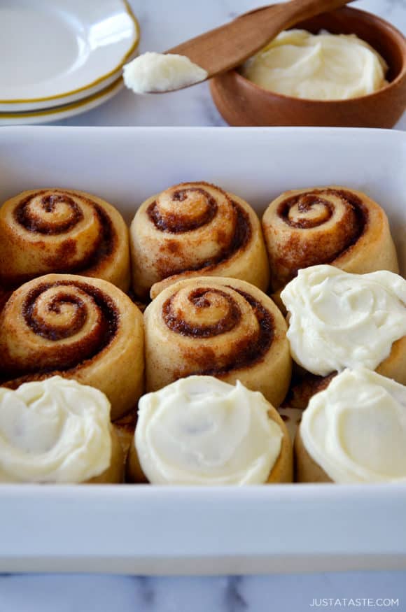 A white baking dish with cinnamon rolls and a bowl of frosting