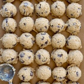 Rows of small scoops of edible cookie dough on brown parchment paper