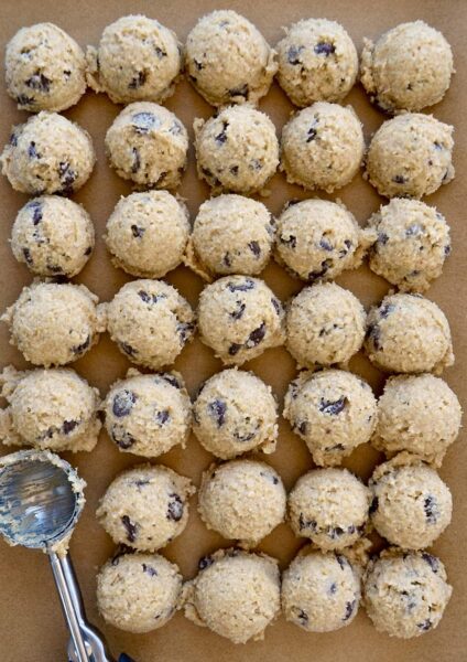 Rows of small scoops of edible cookie dough on brown parchment paper