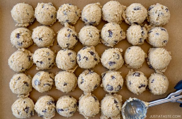 Rows of cookie dough on parchment paper with an ice cream scoop