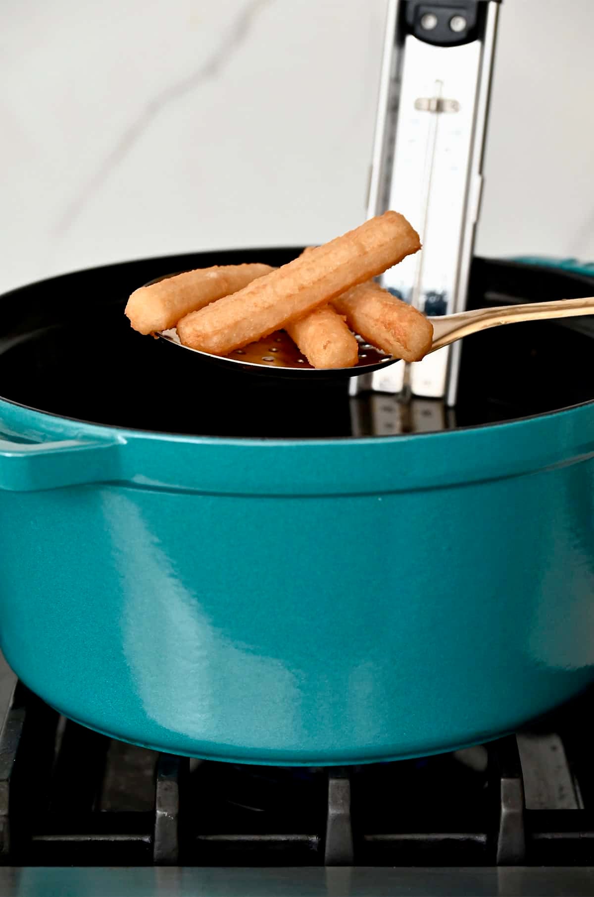 Slotted spoon holding churros over a large stockpot containing deep-fry oil.