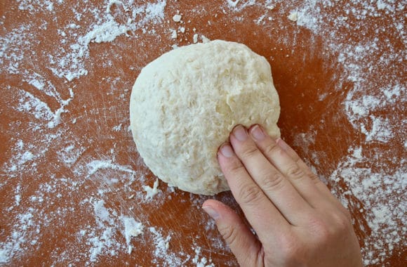 A wood cutting board sprinkled with flour and a ball of pizza dough on top