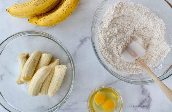 Various sized glass bowls containing halved bananas, flour mixture and eggs