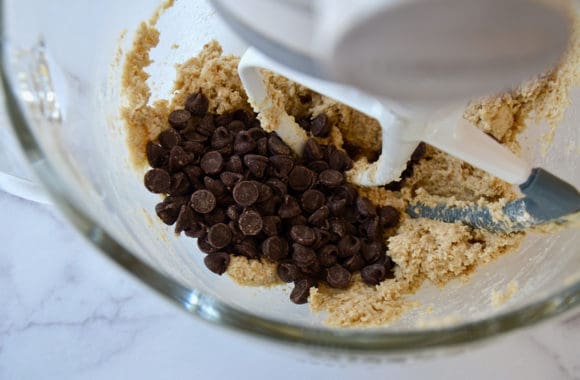 A glass mixing bowl containing chocolate chips and cookie dough