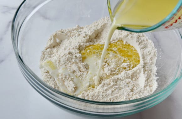 Pouring milk into a clear bowl containing flour and olive oil