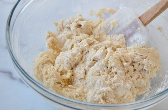 A glass bowl with pizza dough and a spatula