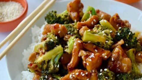 Quick Orange Chicken and Broccoli over white rice in bowl with chopsticks next to a sliced orange