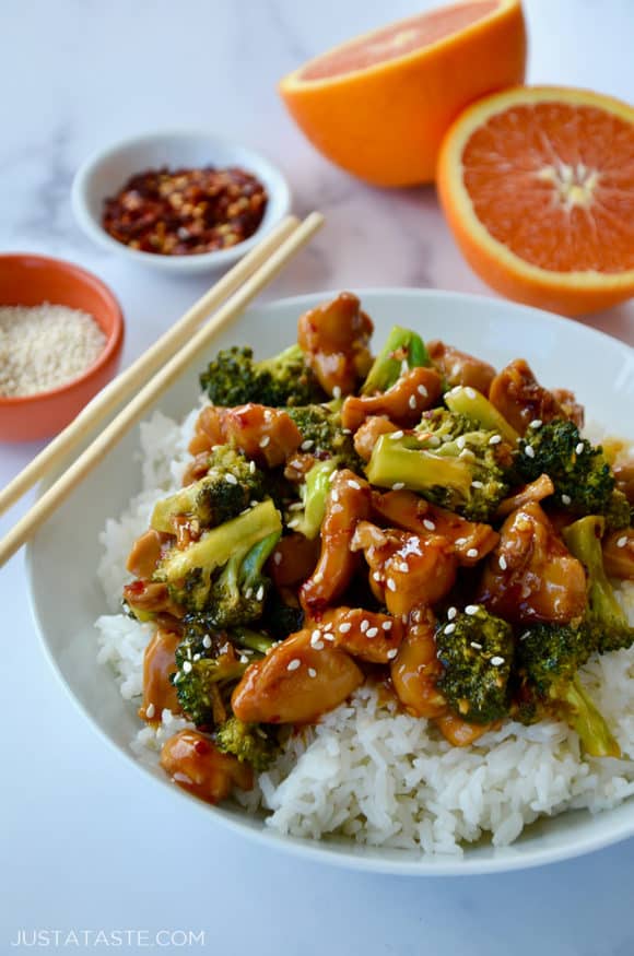 Quick Orange Chicken and Broccoli over white rice in bowl with chopsticks next to a sliced orange