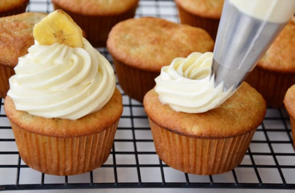 Piping cream cheese frosting on to banana cupcakes