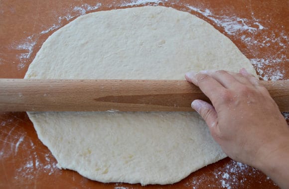 A rolling pin on top of pizza dough on a cutting board