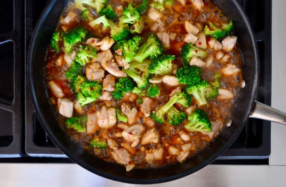 Top down view of large skillet on stove with stir fry ingredients and sauce