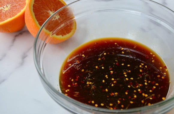 Clear bowl containing stir fry sauce next to a sliced orange