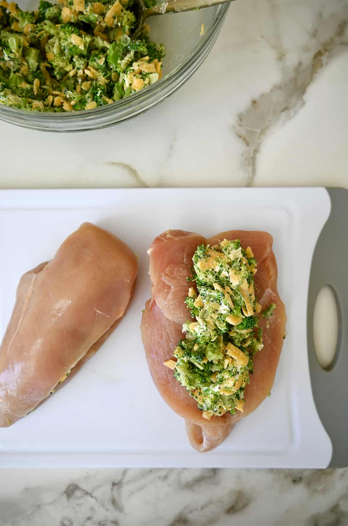 A broccoli and cheese filling stuffed into a raw chicken breast on a cutting board.