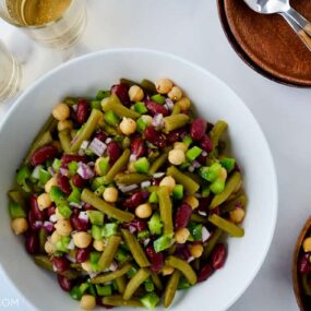 A white bowl with bean salad and plates next to it