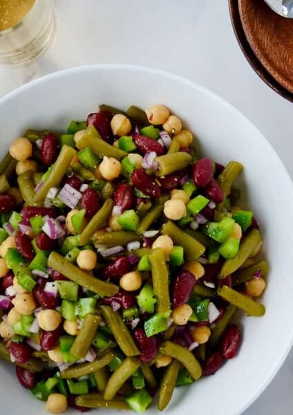 A white bowl with bean salad and plates next to it