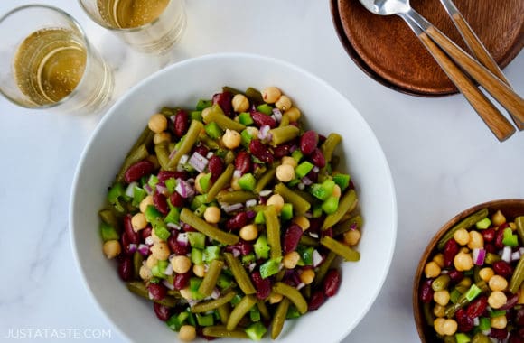 A white bowl with bean salad and plates next to it