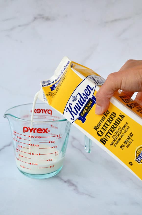 A carton of buttermilk being poured into a glass liquid measuring cup