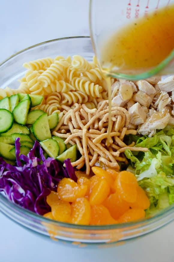 Sesame dressing being poured over salad in large clear bowl