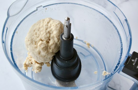 A clear food processor bowl containing balled up dough