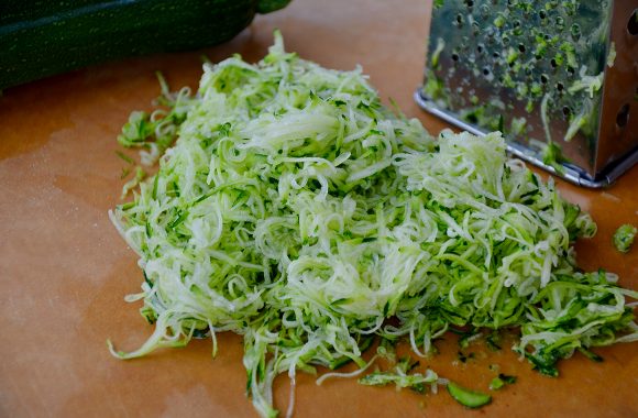 Box grater and shredded zucchini on cutting board