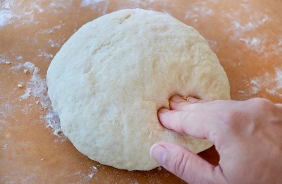 Fingers pressing into a ball of dough on floured surface