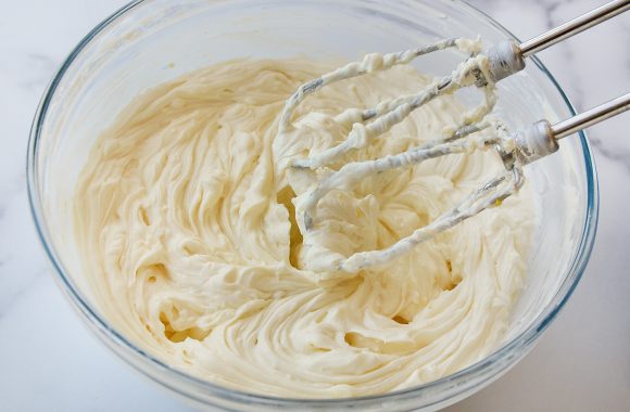 Handheld beater over glass bowl containing creamy cheesecake mixture