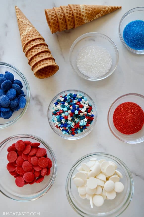 Various sized bowls with red, white, and blue sprinkles and candy melts next to waffle cones