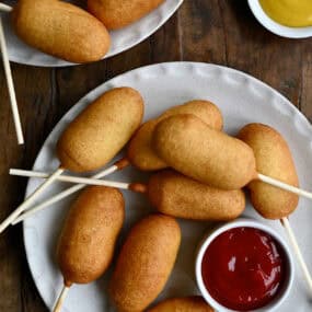 Homemade mini corn dogs on a plate with a small bowl containing ketchup.