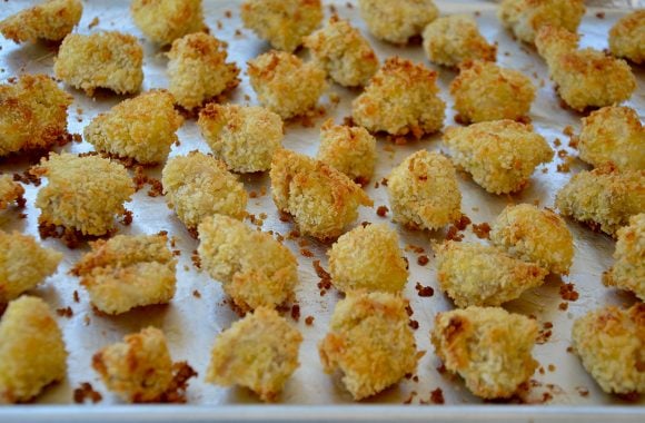 A baking sheet lined with foil containing crispy breaded chicken thigh nuggets