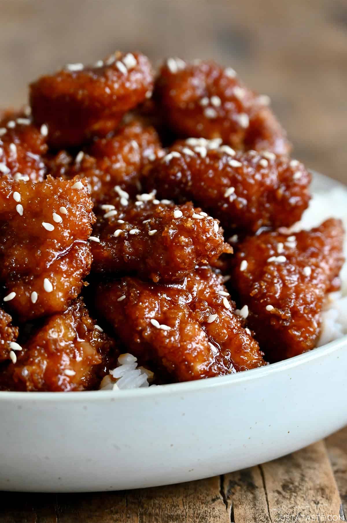 Crispy sesame chicken garnished with sesame seeds on a dinner plate with white rice.