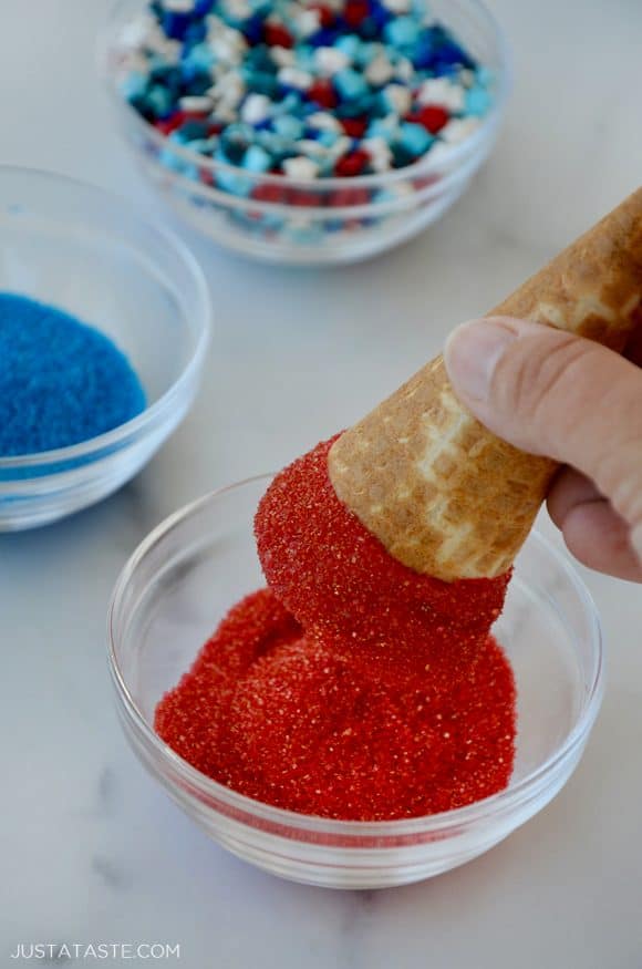 Hand holding waffle cone being dipped in red sprinkles