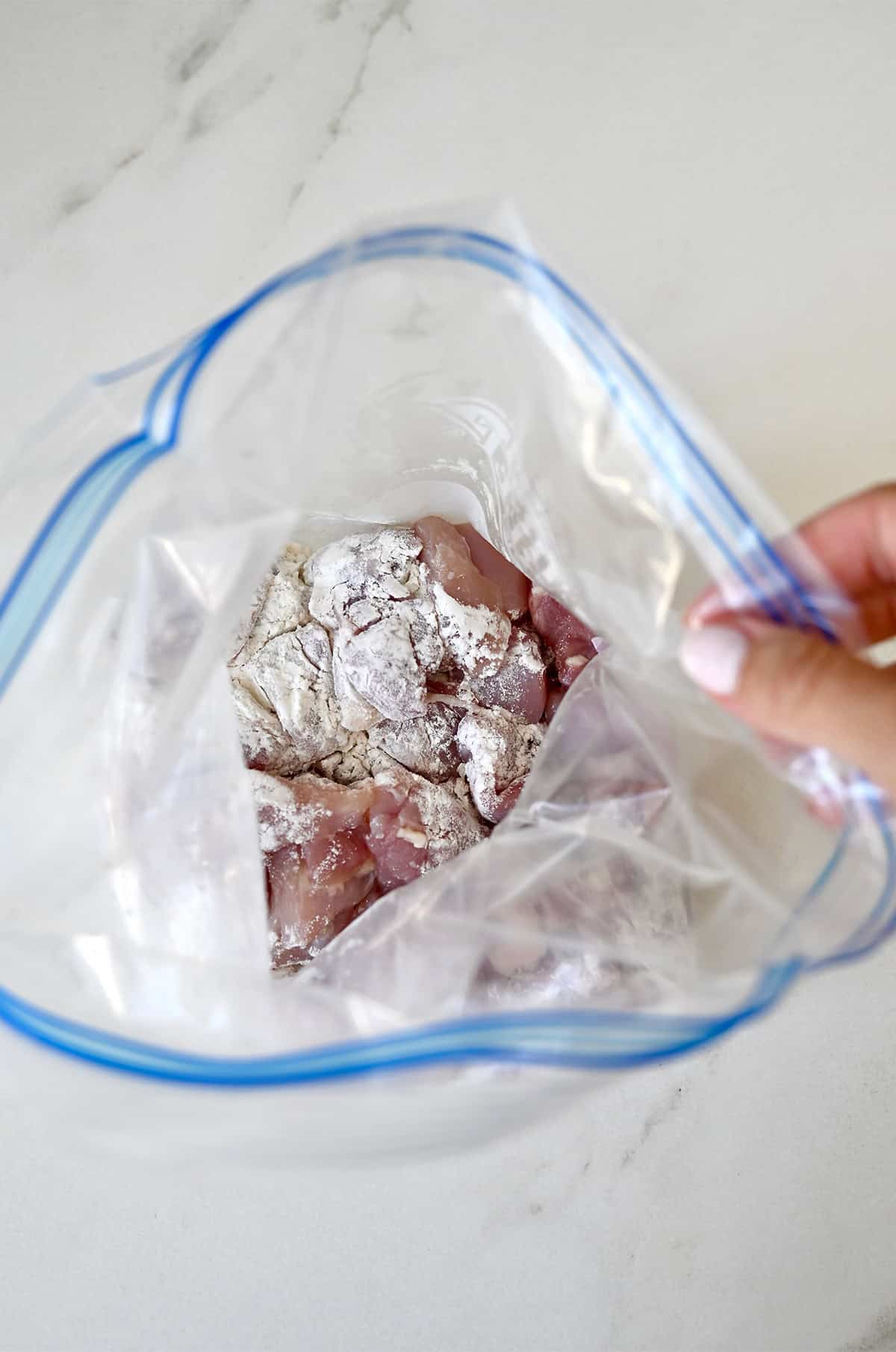 Chicken thigh pieces coated in flour in a sealable plastic bag.