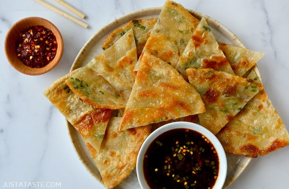 A plate with scallion pancakes cut into wedges and soy dipping sauce