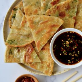 A plate containing scallion pancakes with a white dish of soy dipping sauce and chopsticks