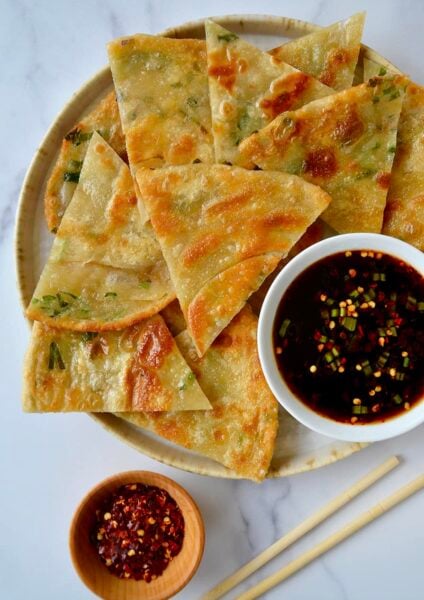 A plate containing scallion pancakes with a white dish of soy dipping sauce and chopsticks