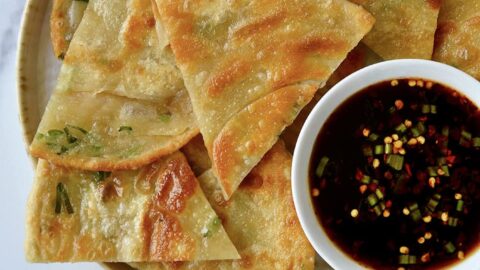 A plate containing scallion pancakes with a white dish of soy dipping sauce and chopsticks