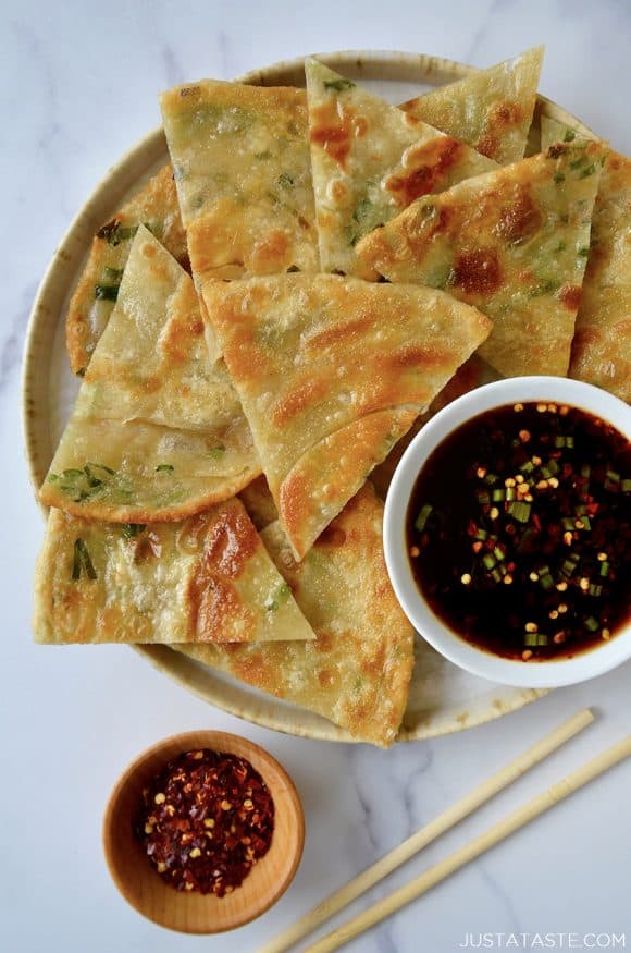 A plate containing scallion pancakes with a white dish of soy dipping sauce and chopsticks