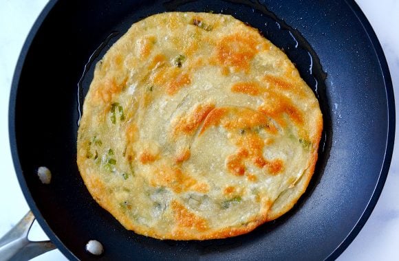 A skillet containing oil and a cooked scallion pancake