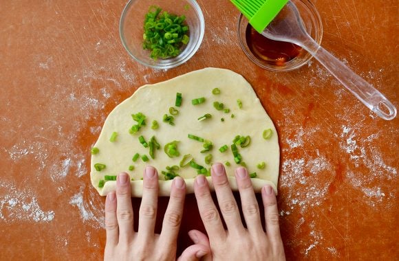 Hand rolling up a scallion pancake brushed with sesame oil
