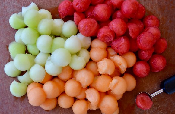 Melon baller next to cantaloupe balls, honeydew melon balls and watermelon balls