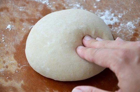 A hand pushing into a ball of dough on a cutting board