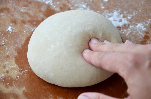A hand pushing into a ball of dough on a cutting board