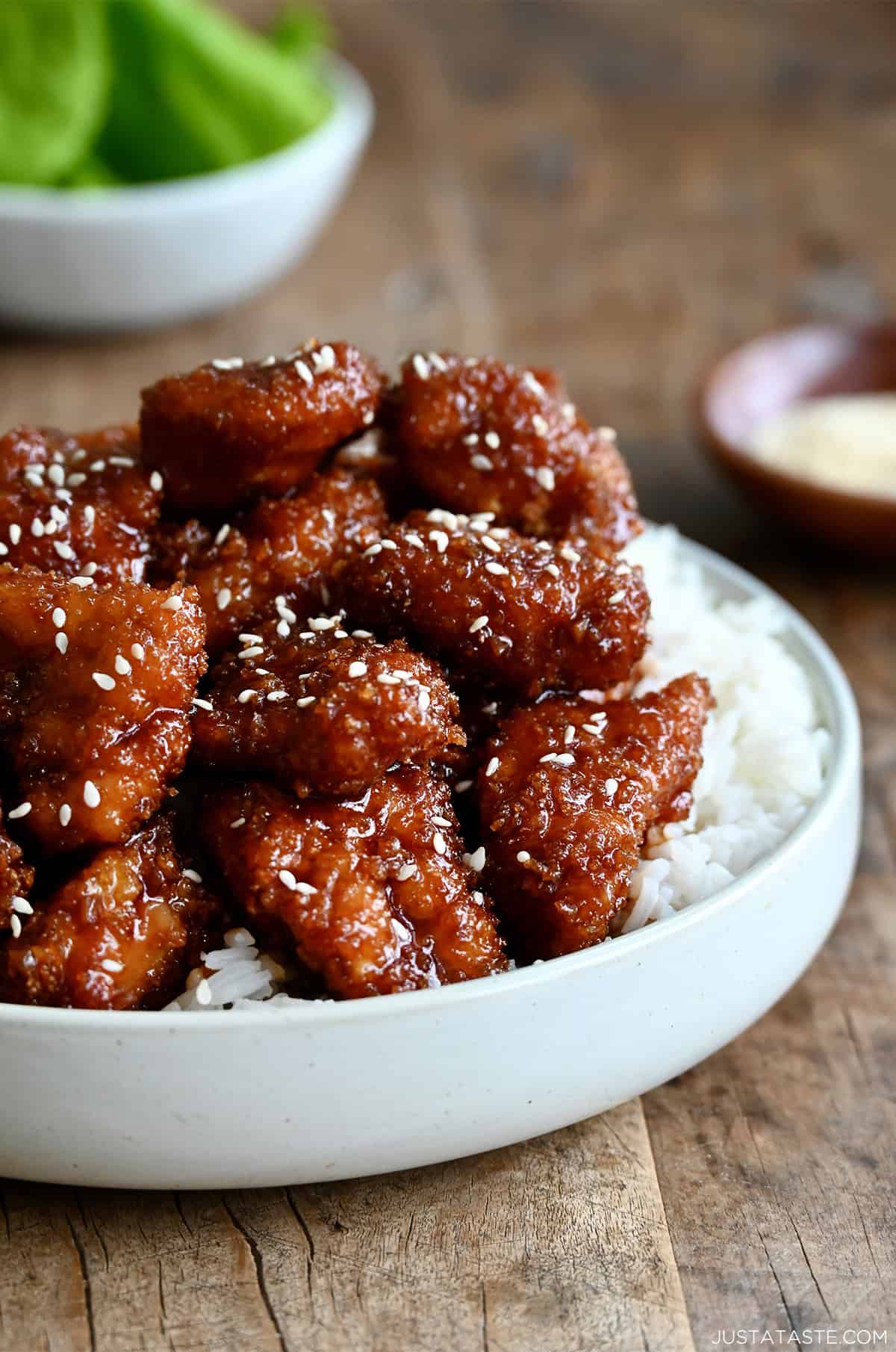 Crispy sesame chicken topped with sesame seeds over white rice on a dinner plate.