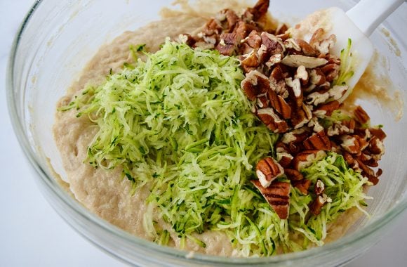 Glass bowl containing shredded zucchini, chopped pecans and muffin batter