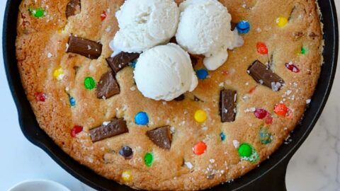 Leftover Halloween Candy Skillet Cookie topped with vanilla ice cream next to small bowls containing chocolate candy