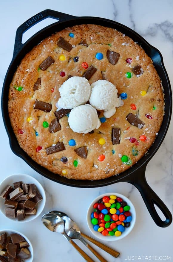 Leftover Halloween Candy Skillet Cookie topped with vanilla ice cream next to small bowls containing chocolate candy