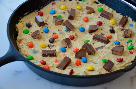 Cast iron skillet containing unbaked cookie dough topped with chopped candy