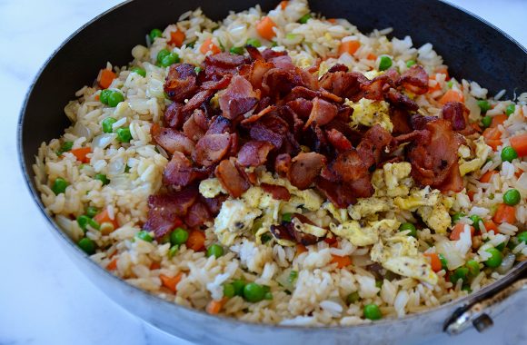 Large skillet with peas, carrots, onions, rice, eggs and bacon