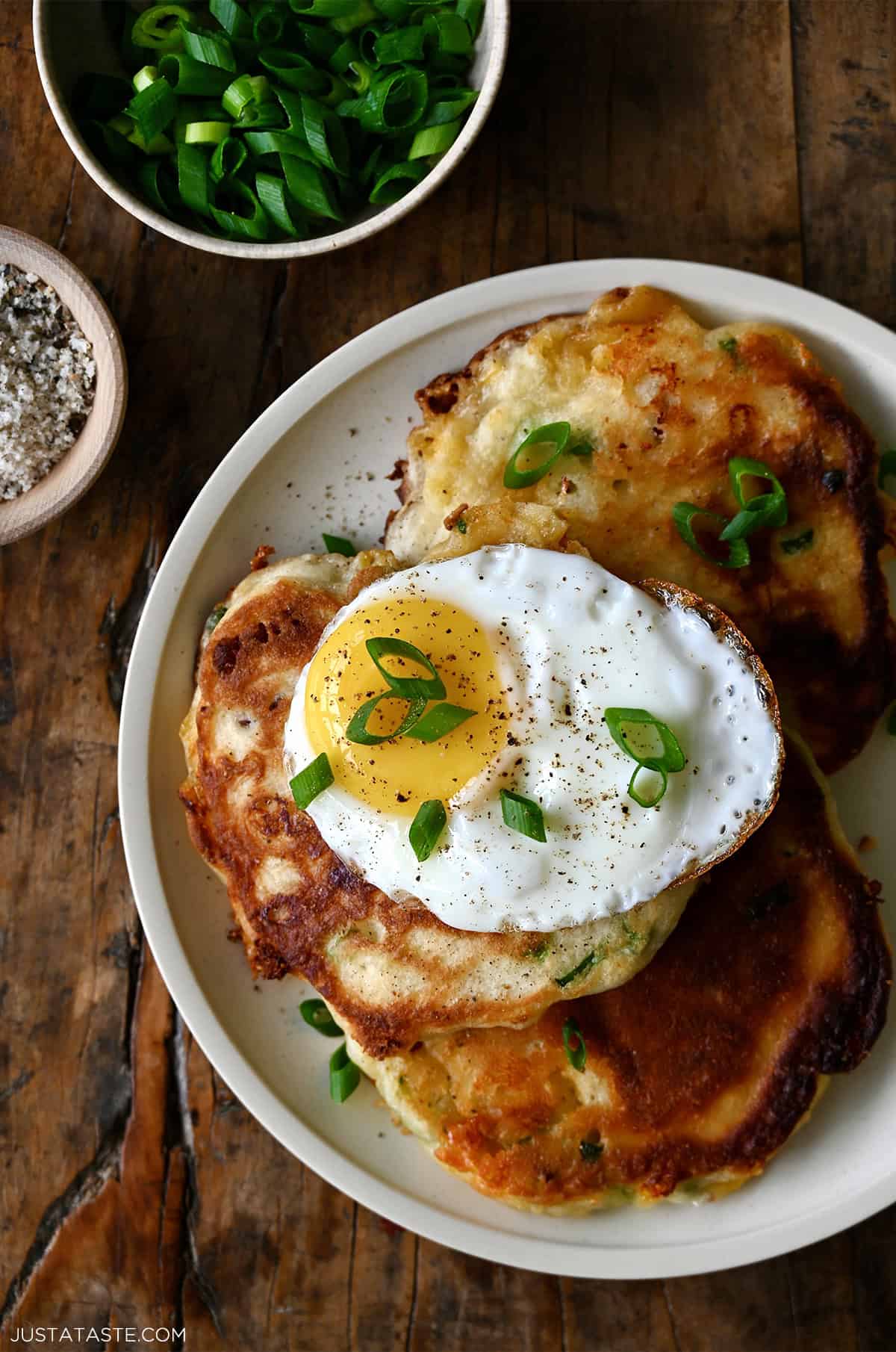 Savory pancakes with bacon and cheese topped with a fried egg and sliced scallions.