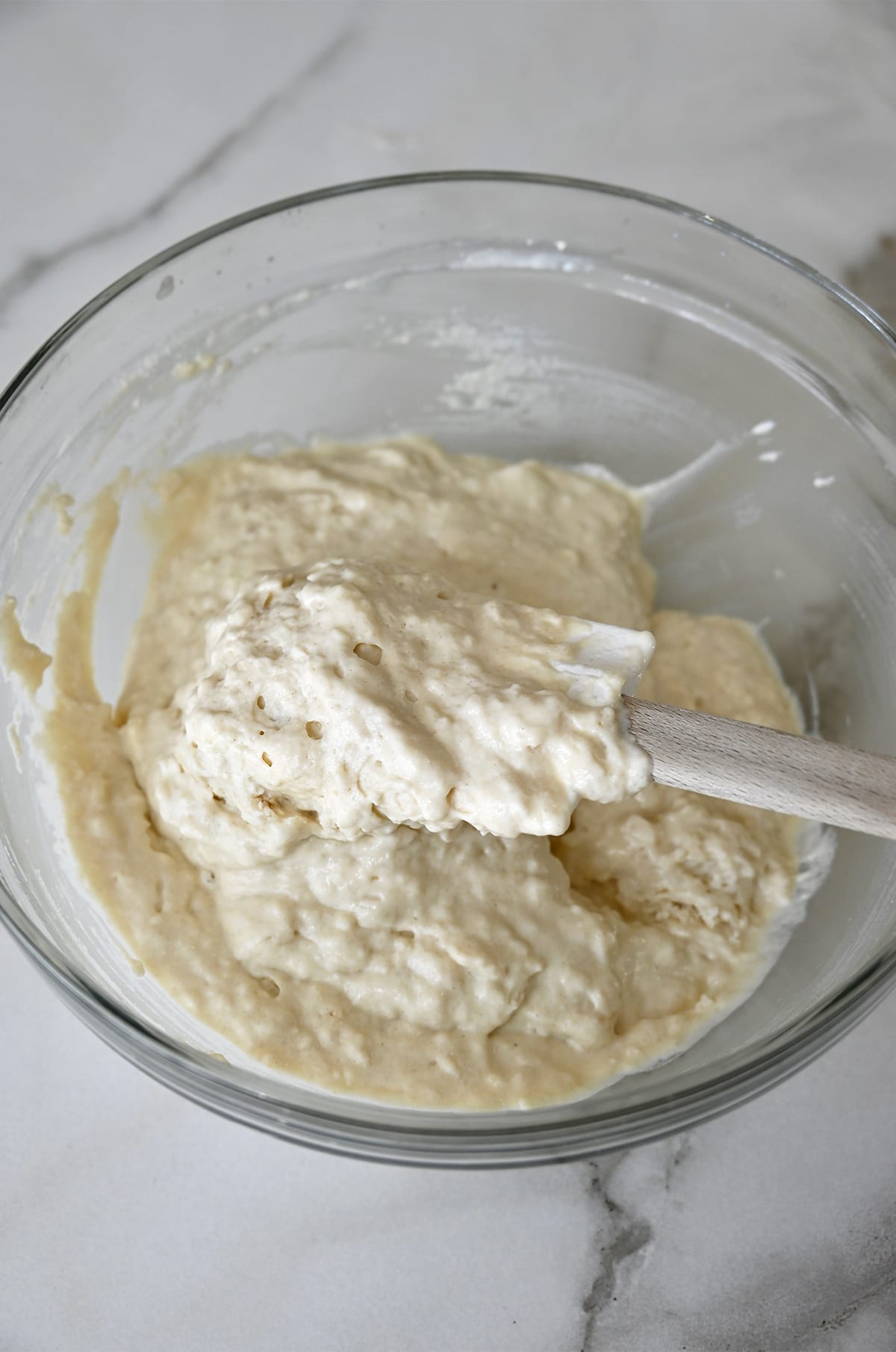 Thick buttermilk pancake batter in a glass bowl with a spatula.